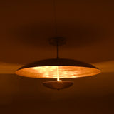 Warm brass ceiling light with bowl-shaped lower disc illuminated in a dark room