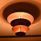Warm glowing bottom view of the multi-tier brass flushmount chandelier, highlighting indirect lighting and dramatic shadow patterns.