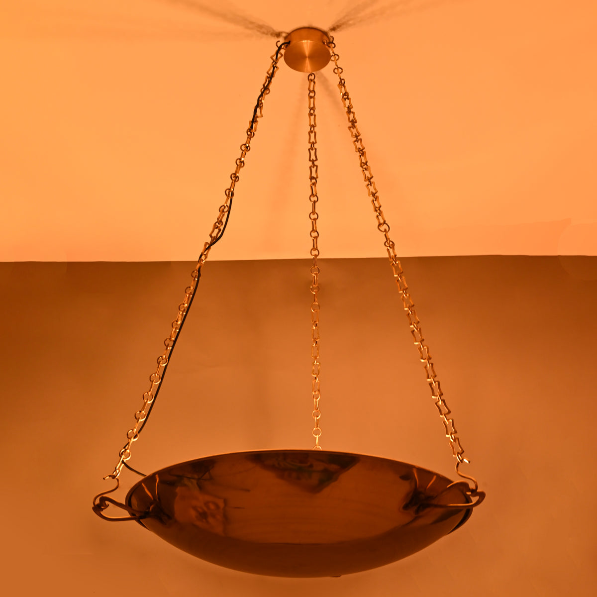 Dark-room view of brass bowl pendant showcasing warm reflective brass glow and chain details