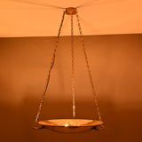 Brass bowl pendant light hanging from chains, glowing warmly in a dim interior