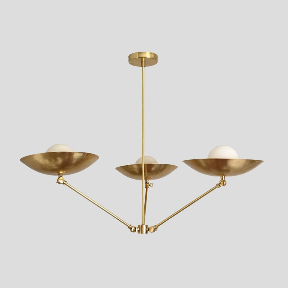 Side view of brass chandelier with three frosted globes and bowl shades, handmade ceiling pendant with minimalist industrial design.