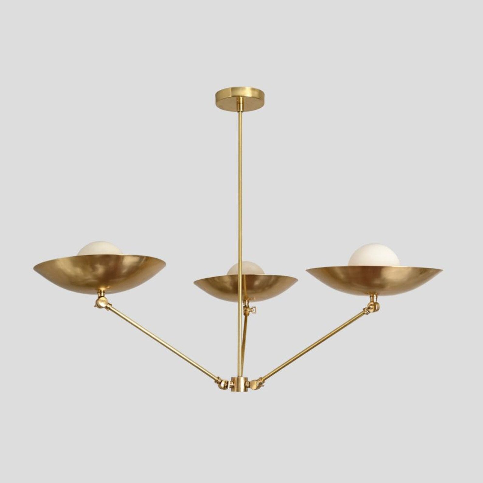 Side view of brass chandelier with three frosted globes and bowl shades, handmade ceiling pendant with minimalist industrial design.
