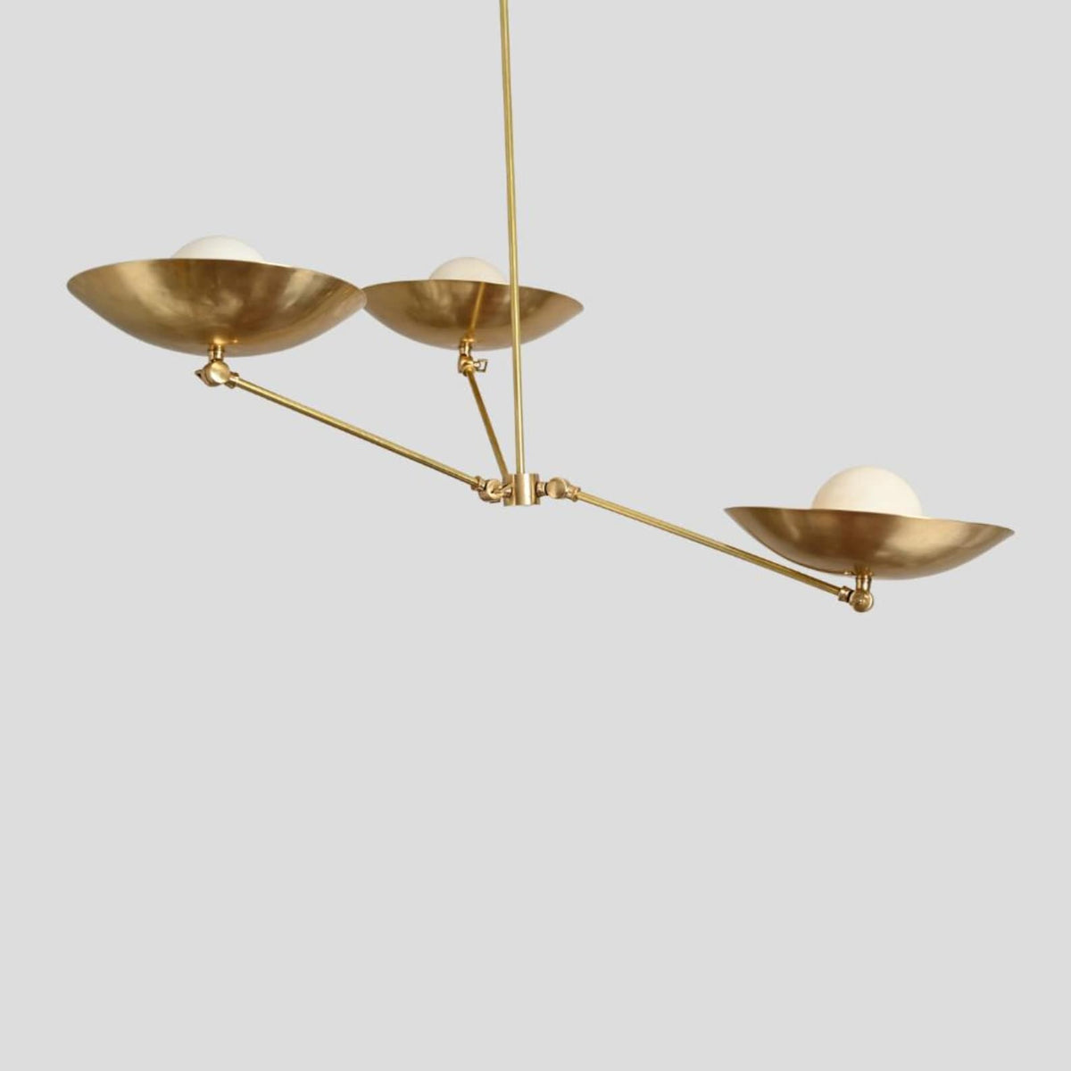 Overhead view of brass pendant chandelier with three frosted globe bulbs set in bowl-shaped brass shades, minimalist ceiling lighting.
