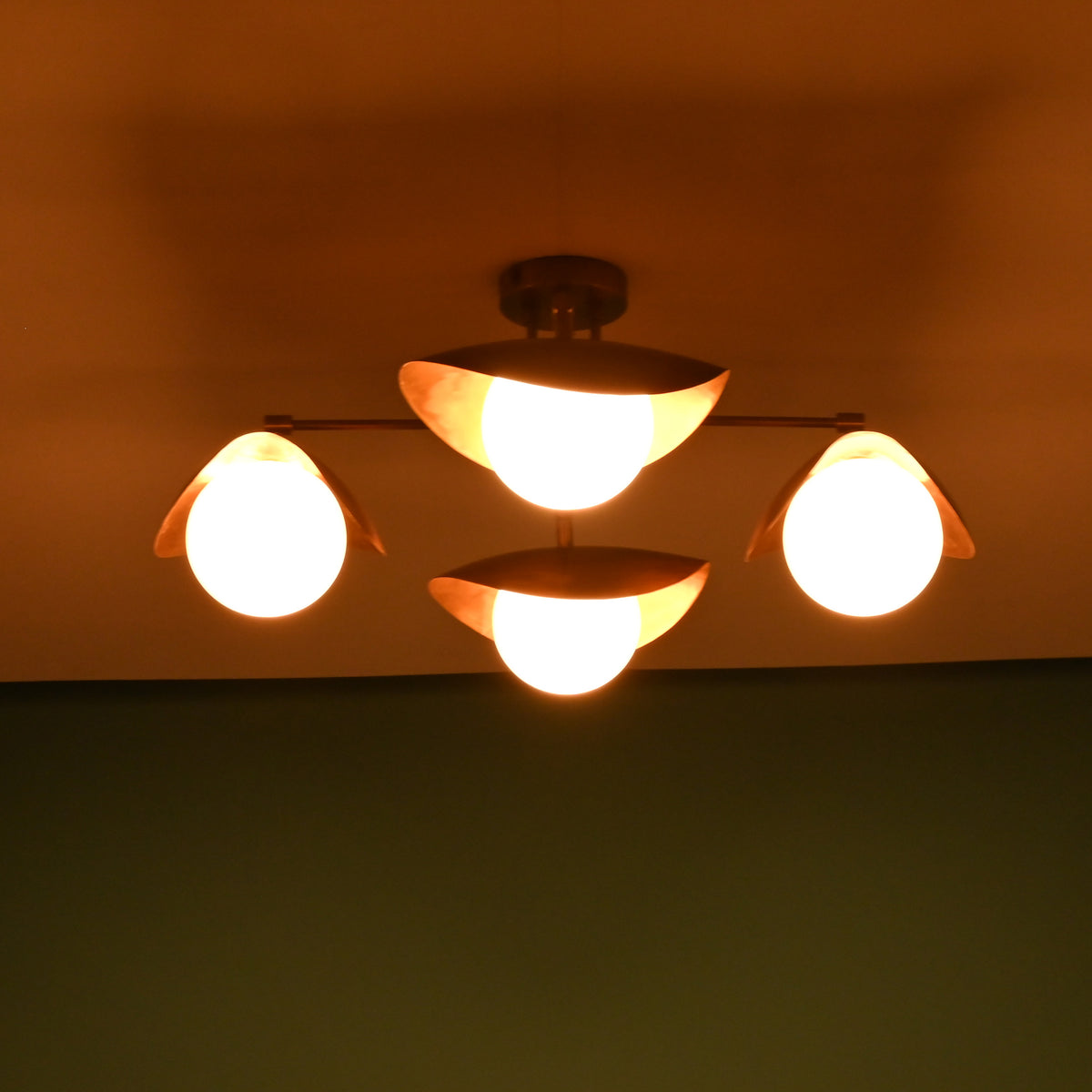 Warm brass flush mount ceiling light with glowing frosted glass shades in a dark setting.