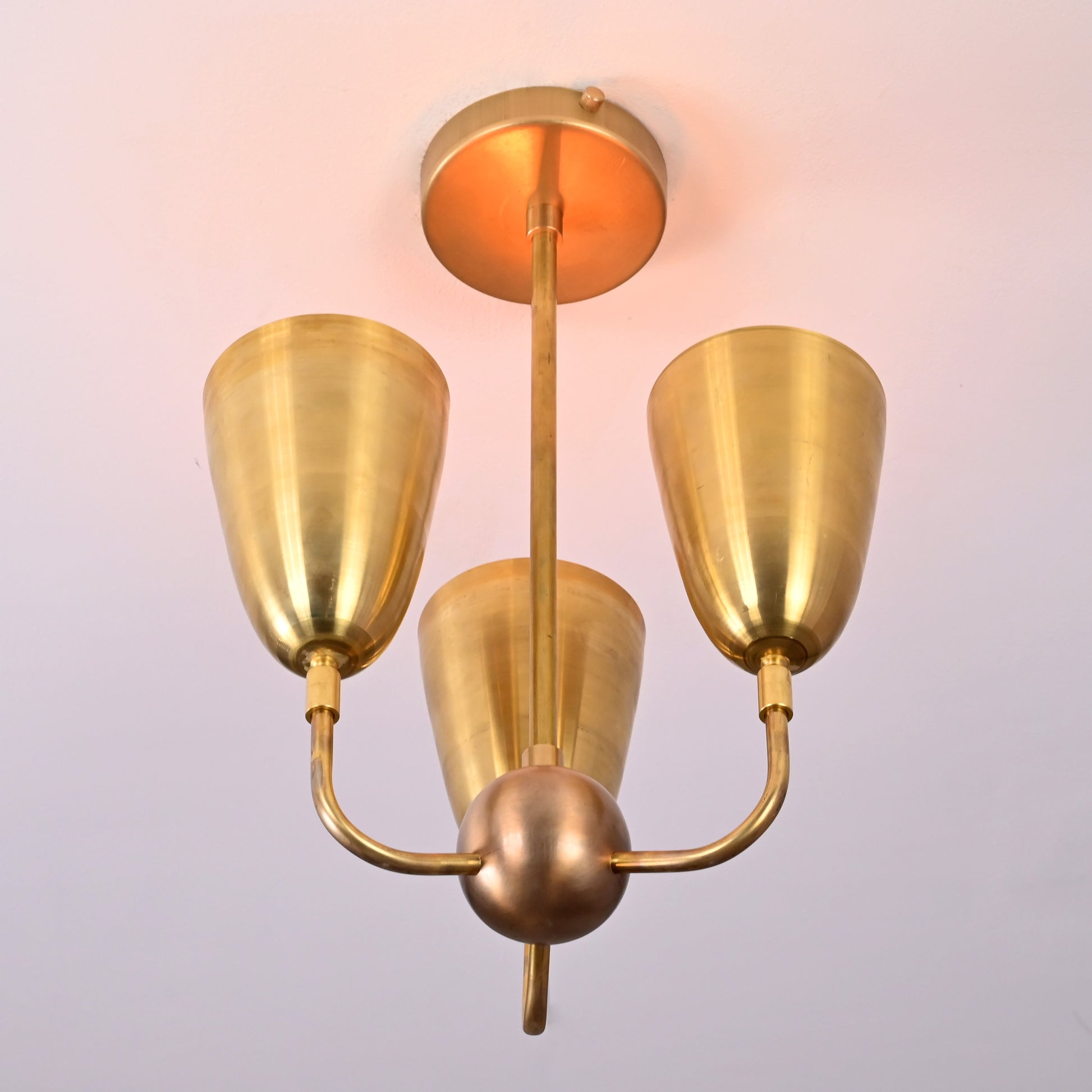 Ceiling light glowing warmly with raw brass finish and cone-shaped reflectors