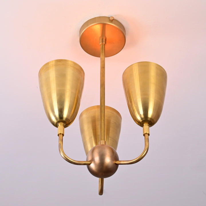 Ceiling light glowing warmly with raw brass finish and cone-shaped reflectors