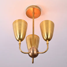 Ceiling light glowing warmly with raw brass finish and cone-shaped reflectors