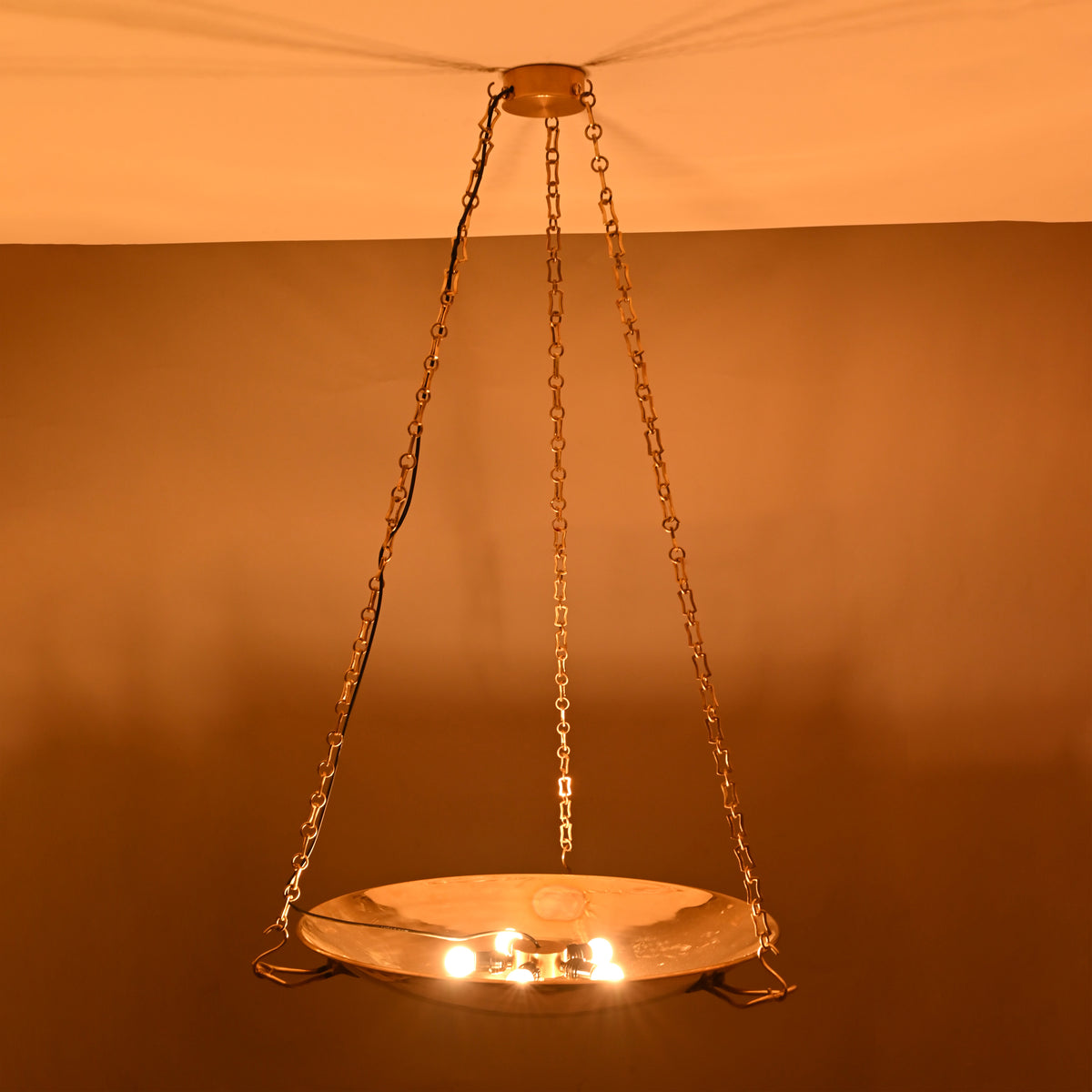 Night view of brass bowl chandelier showing soft uplighting and chain-supported design