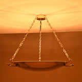 Brass bowl chandelier glowing warmly with indirect ceiling illumination and decorative brass chains