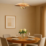 Modern brass disc chandelier above round dining table in warm-toned room, providing ambient lighting for contemporary interiors