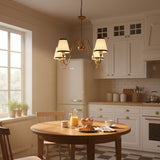 Detailed view of 4-light brass chandelier with elegant curved arms, cream fabric lampshades, and black trim accents