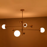 Side angle of illuminated brass chandelier showing warm glowing opal globes and modern linear form.