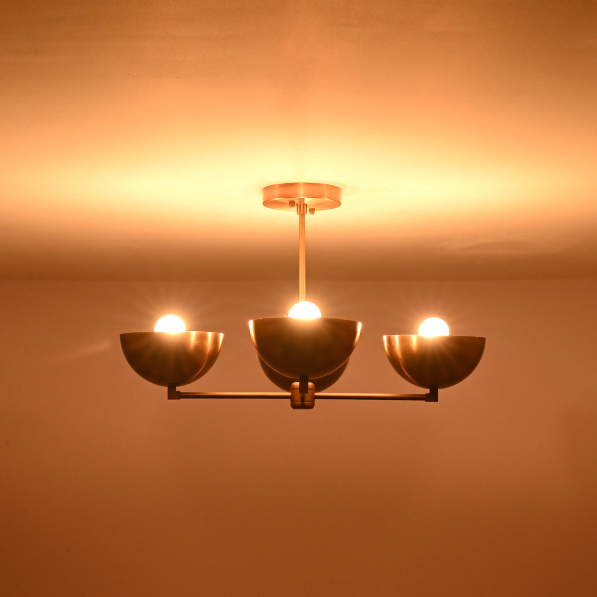 4-bowl brushed brass chandelier illuminated with three glowing bulbs, casting warm indirect light