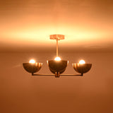 4-bowl brushed brass chandelier illuminated with three glowing bulbs, casting warm indirect light