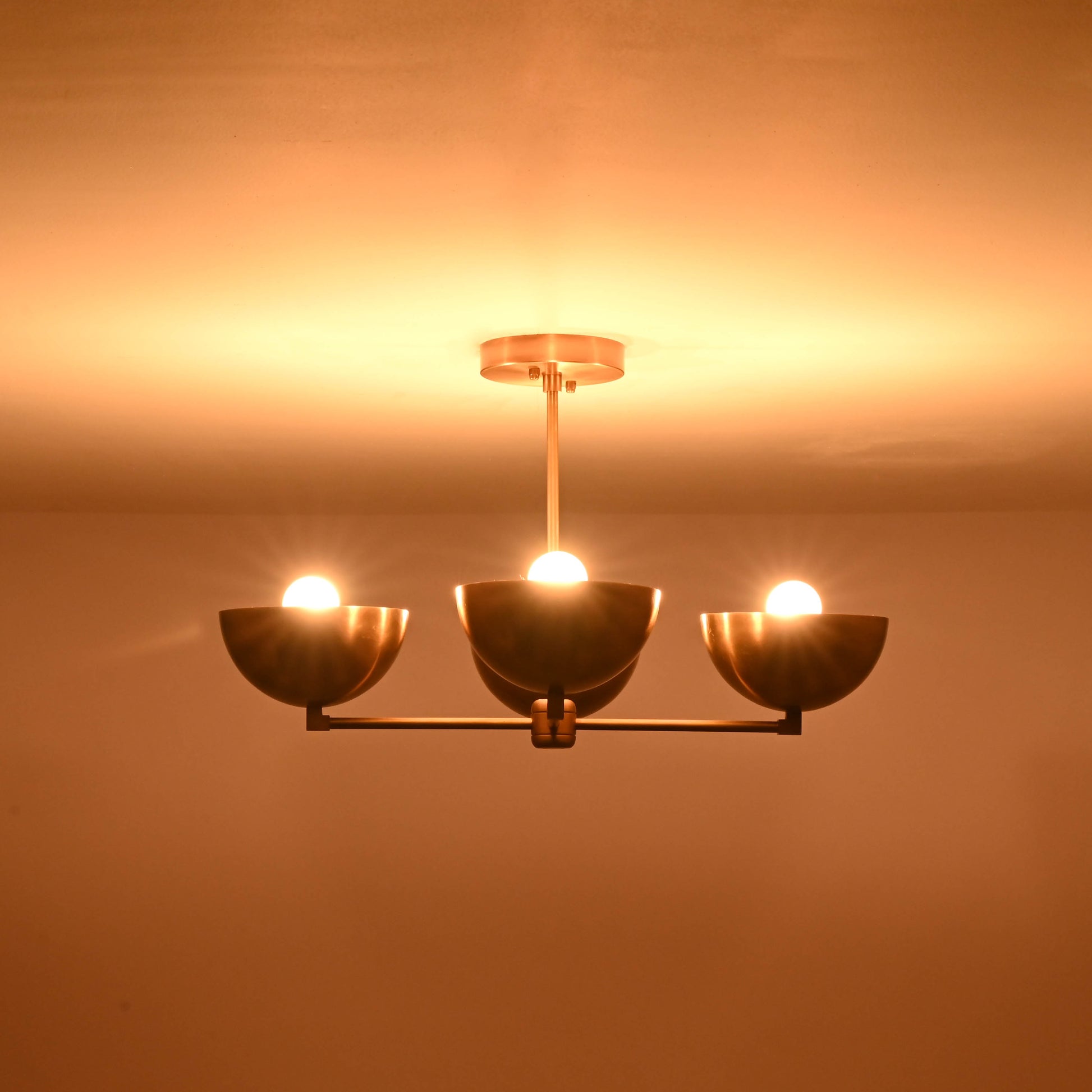 4-bowl brushed brass chandelier illuminated with three glowing bulbs, casting warm indirect light