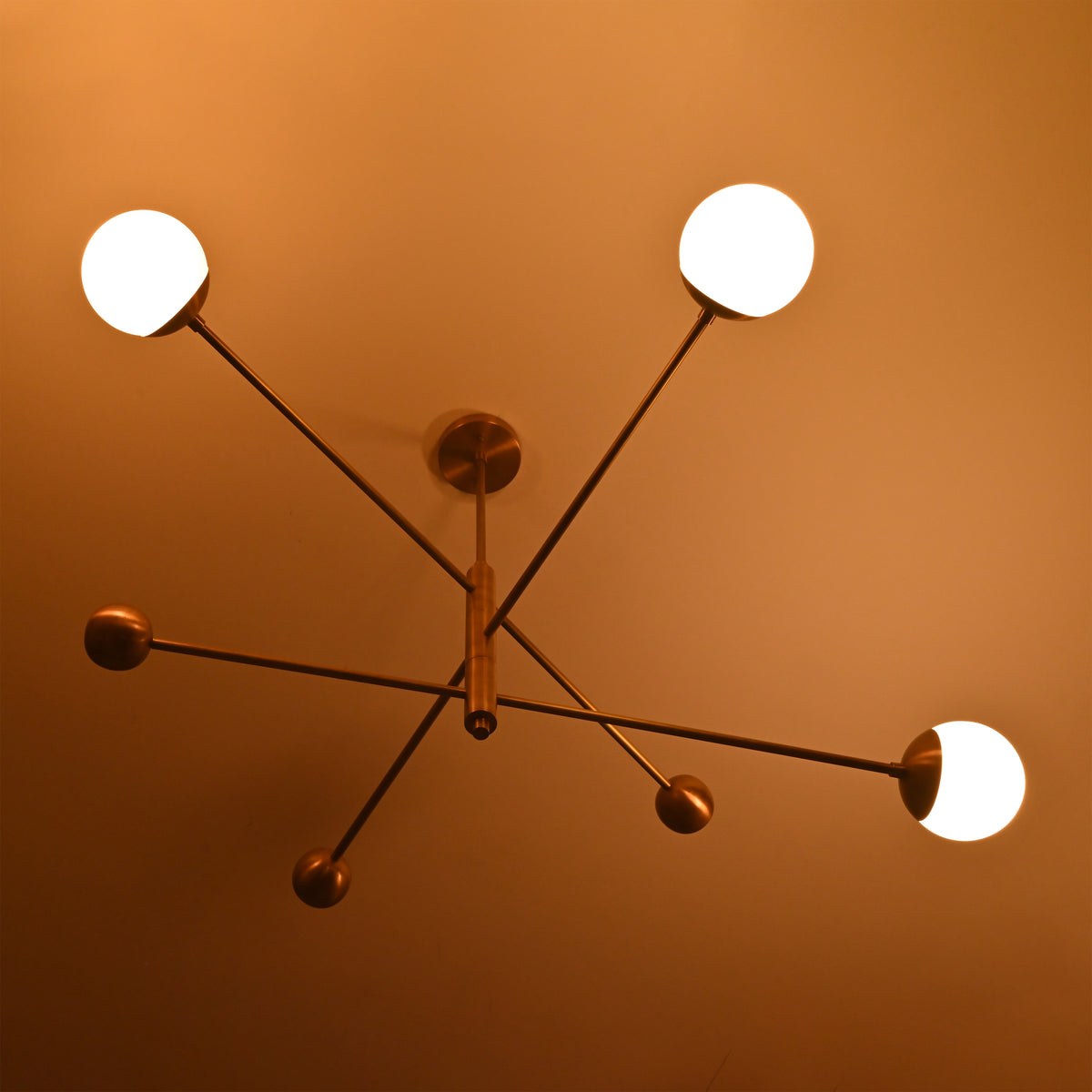 Night view of handcrafted brass chandelier with three illuminated globes, creating soft warm ambient lighting.