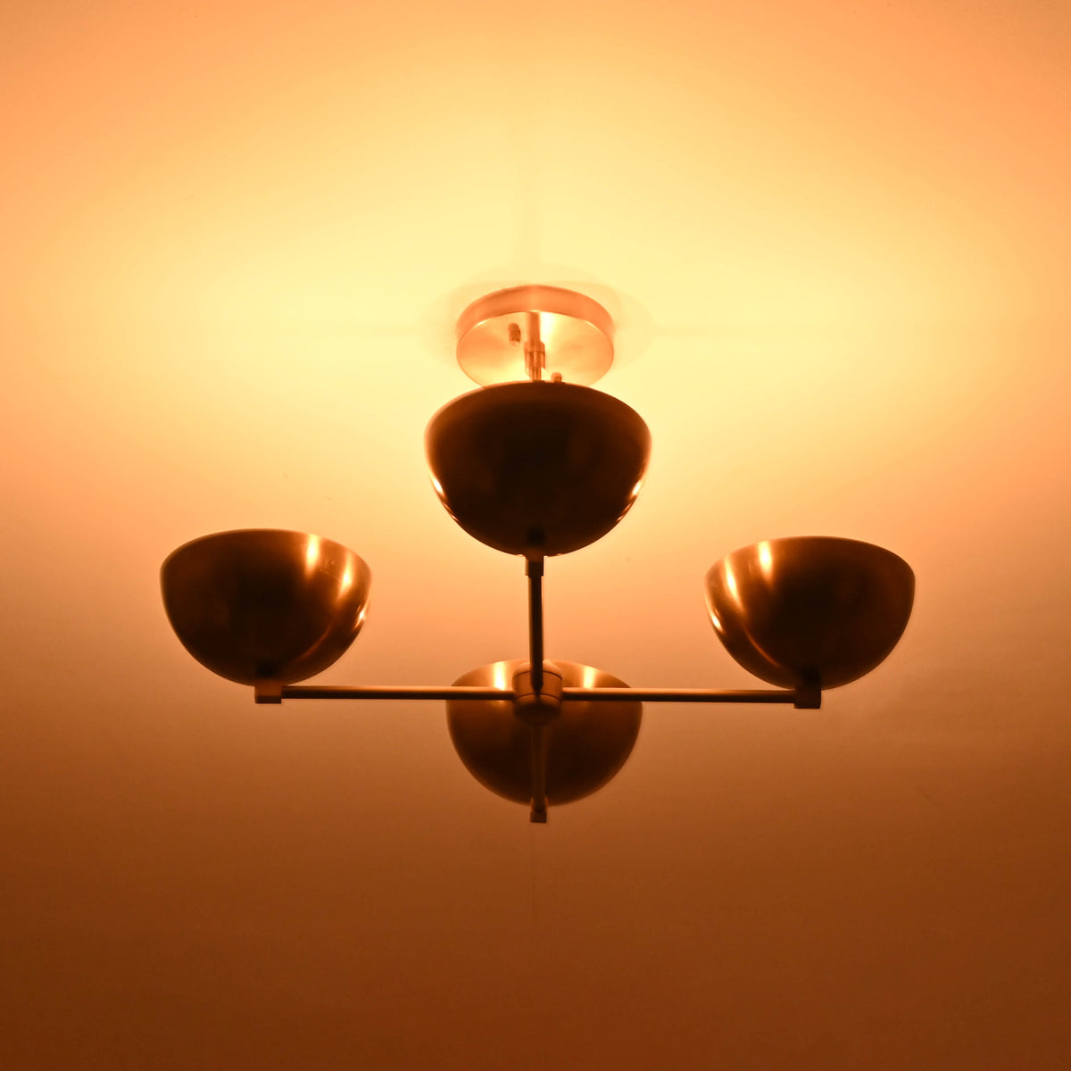 Golden brass chandelier with four bowl shades glowing warmly and casting ambient ceiling light