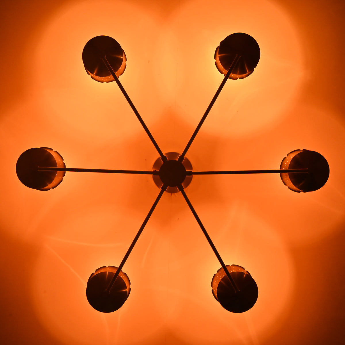 Ceiling light pattern created by perforated brass cone shades casting warm decorative glow in a handcrafted chandelier.