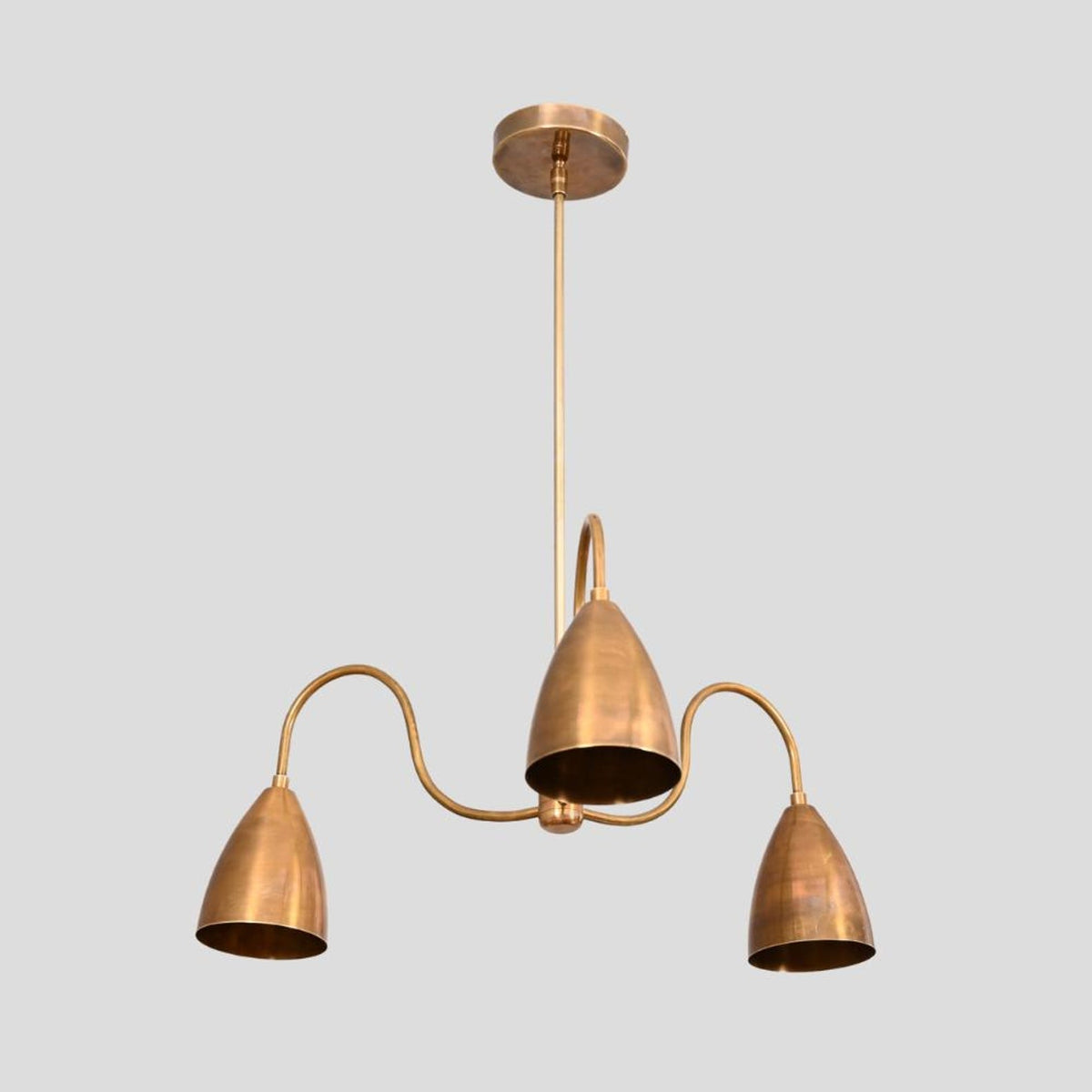 Side angle of handcrafted brass chandelier featuring three cone shades with brushed finish and elegant curved arms.