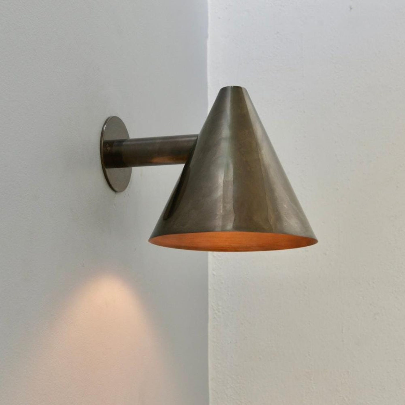 Handmade brass cone wall sconce with minimalist conical shade casting downward light