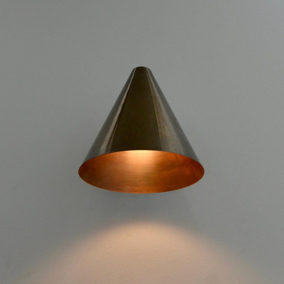 Brass cone wall sconce with wide conical shade creating warm focused illumination