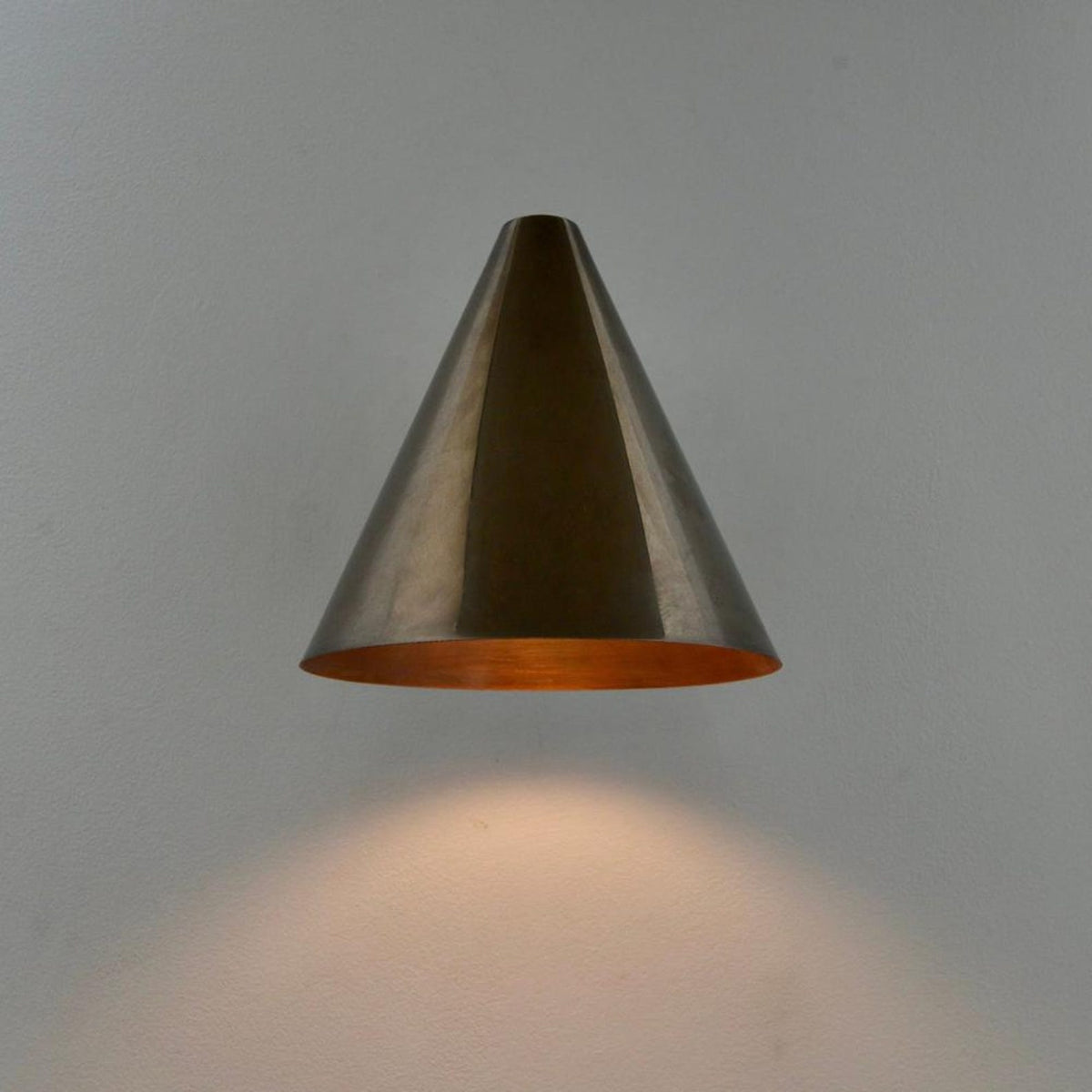 Modern brass wall sconce with cone shade producing soft downward light