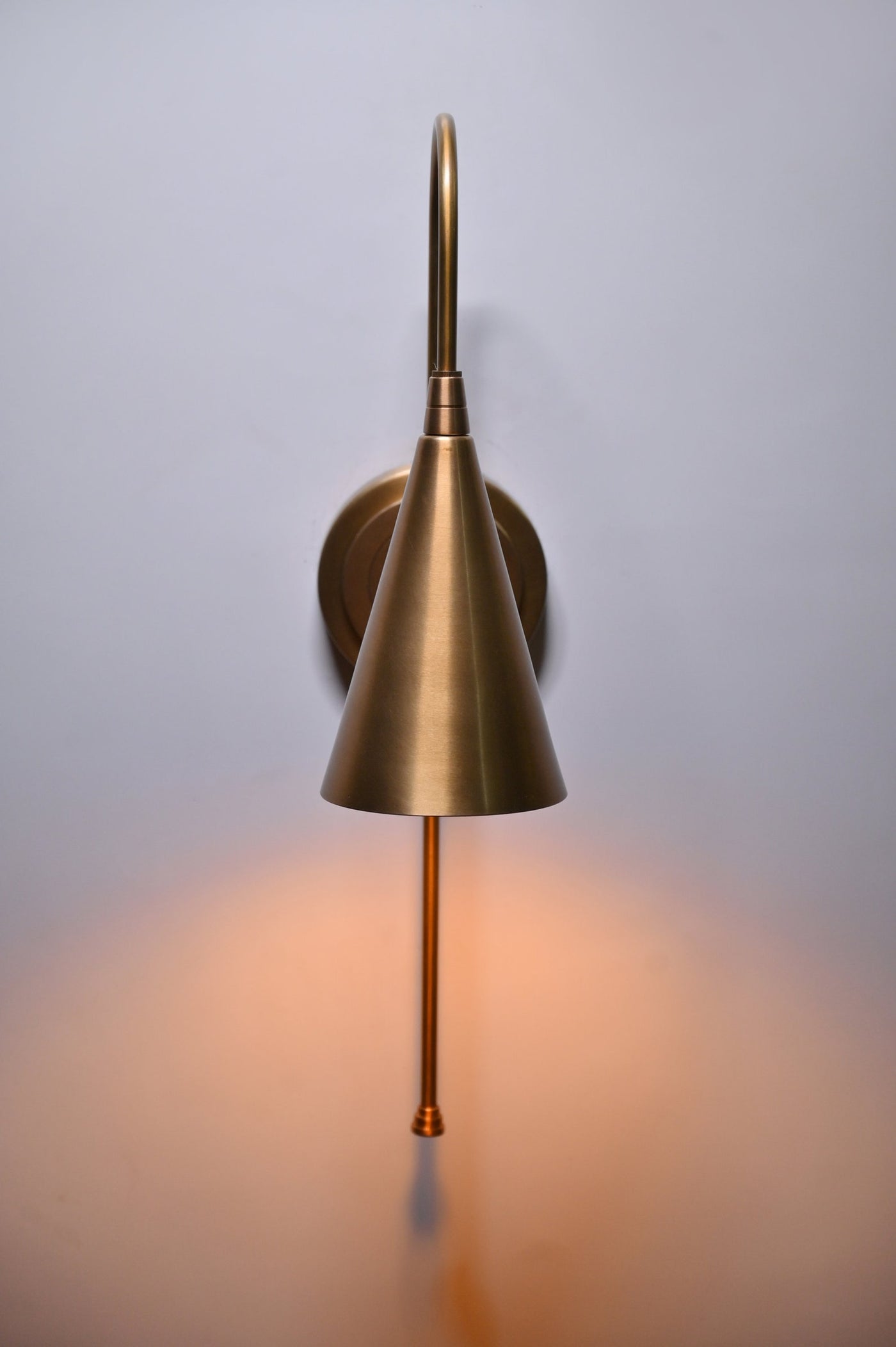 Front view of handmade brass wall sconce with cone shade emitting warm light