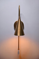 Front view of handmade brass wall sconce with cone shade emitting warm light