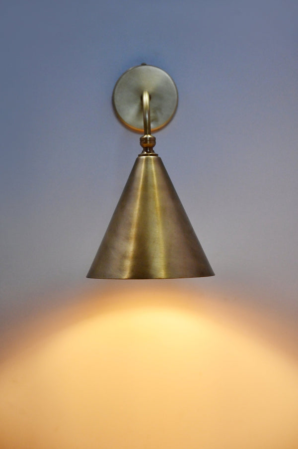 Handmade brass cone wall sconce illuminated on wall, modern minimalist lighting by Brass Leaf Studio