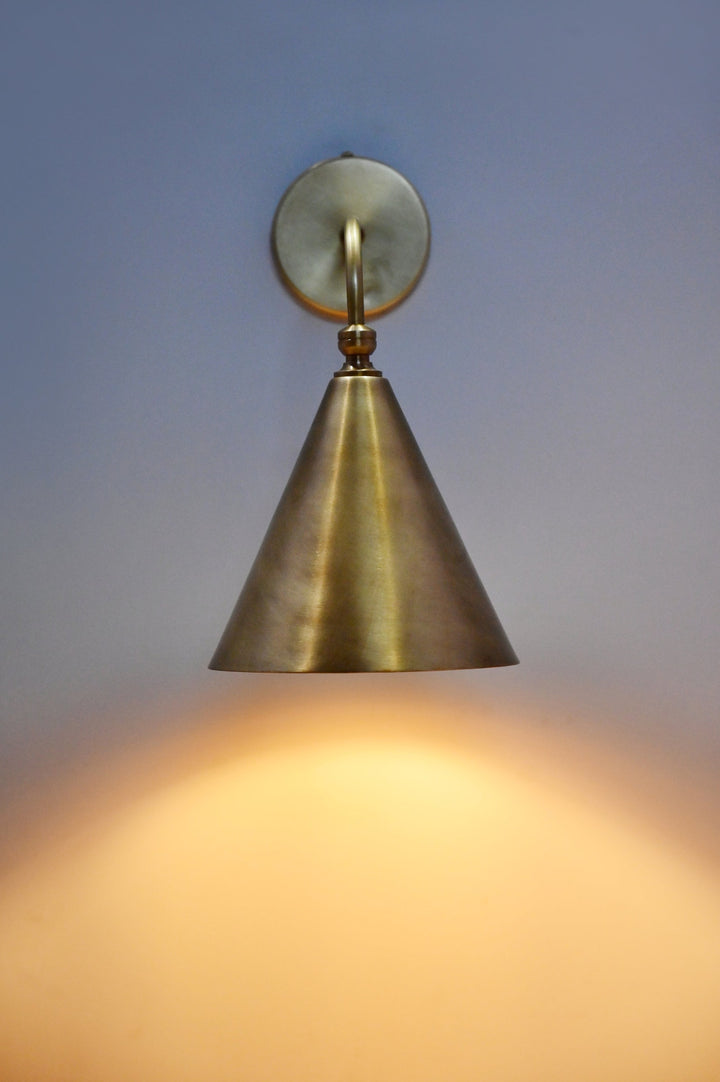 Handmade brass cone wall sconce illuminated on wall, modern minimalist lighting by Brass Leaf Studio