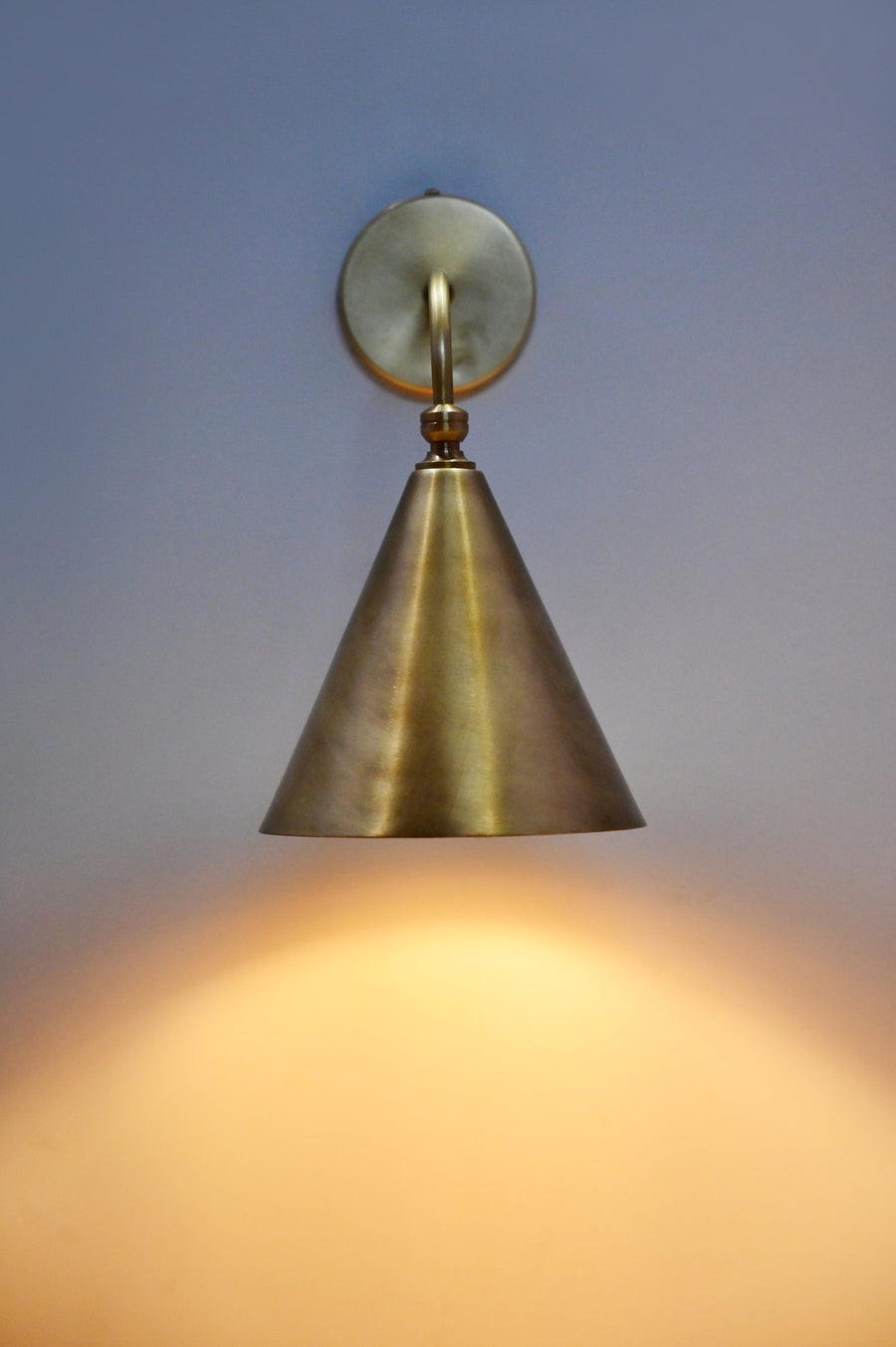 Handmade brass cone wall sconce illuminated on wall, modern minimalist lighting by Brass Leaf Studio