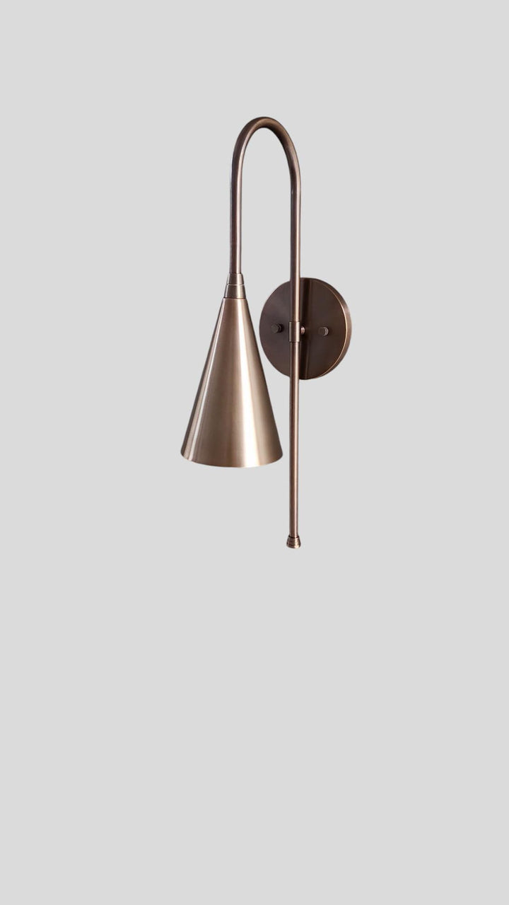 Side angled view of brass cone shade wall sconce with curved arm design
