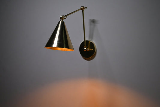 Brass cone wall sconce illuminated in dark room, warm ambient lighting