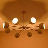 Illuminated 8-light brass chandelier glowing warmly with cream dome shades for ambient lighting