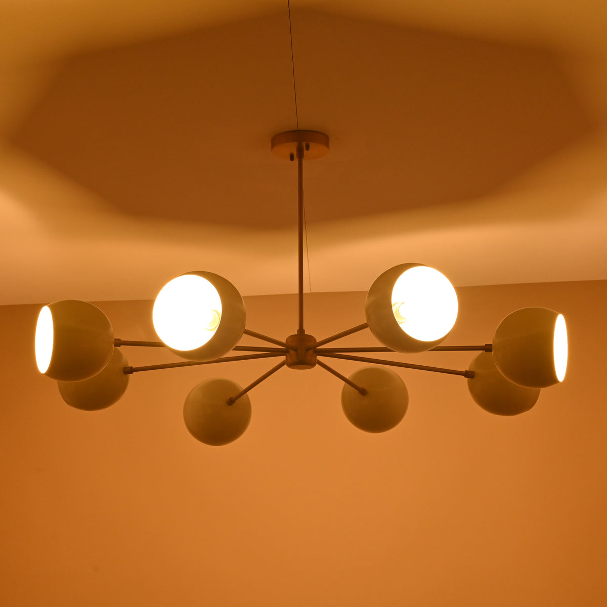 Modern brass chandelier with eight cream domes casting warm light across the ceiling