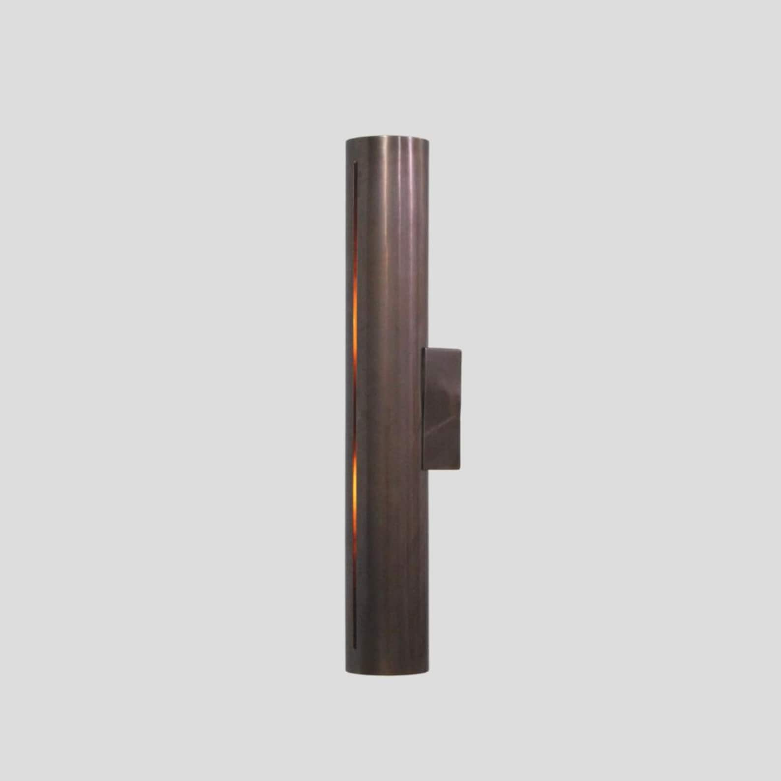 Handmade brass cylinder wall sconce light with warm glow, minimalist industrial design, crafted by Brass Leaf Studio.