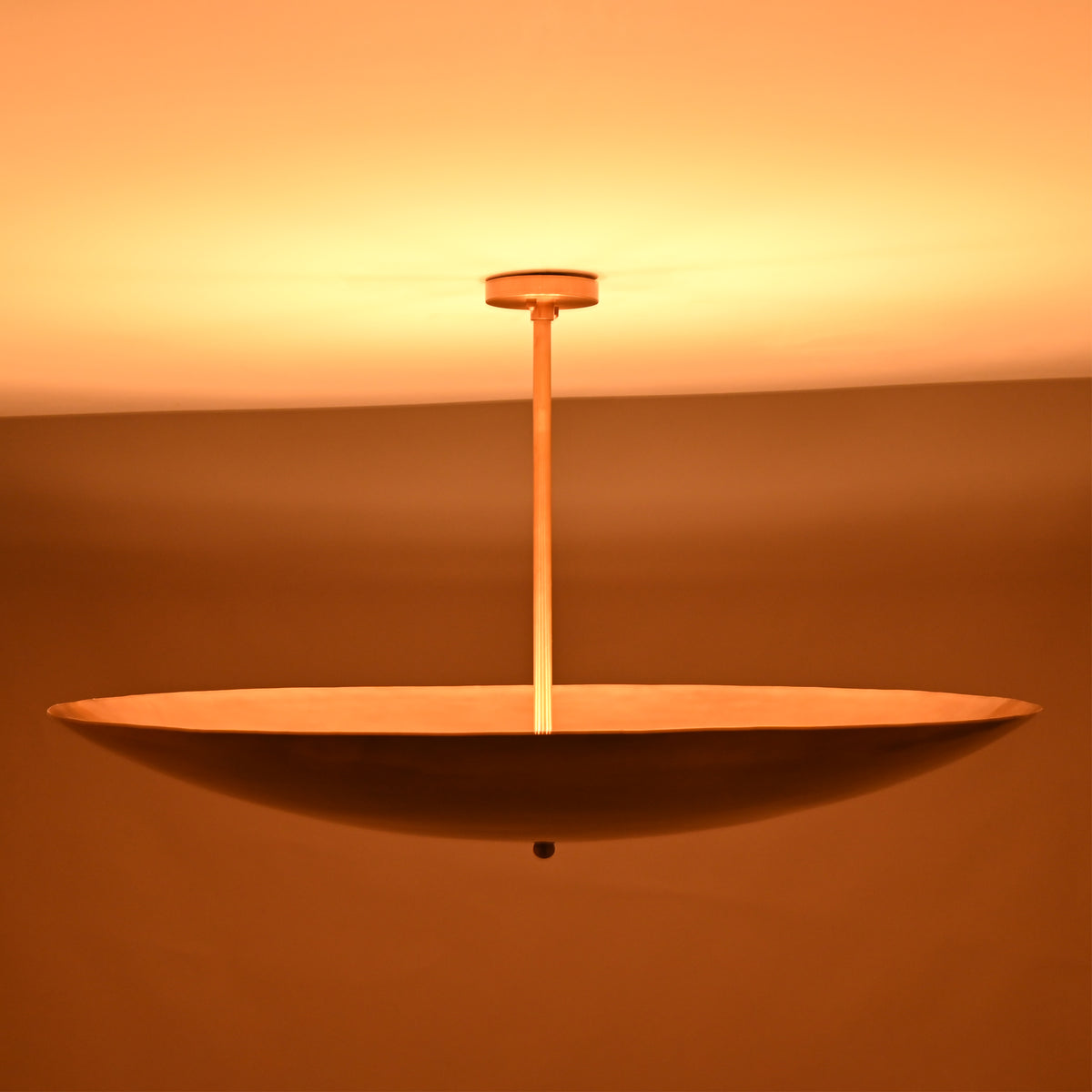 Minimalist brass disc light viewed from below, creating soft upward illumination and warm ambient tones.