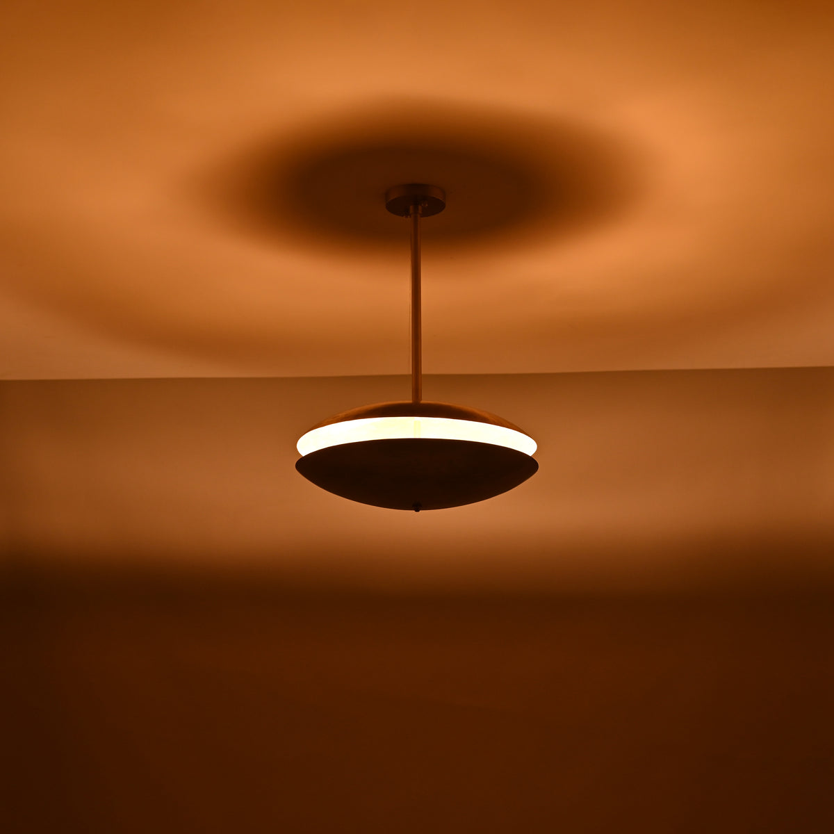Wide-view shot of brass disc chandelier in a dark room, casting a soft halo of warm indirect light across the ceiling.