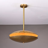 Brass disc chandelier illuminated from within, showing warm golden glow highlighting the textured hammered brass finish and sculptural form.