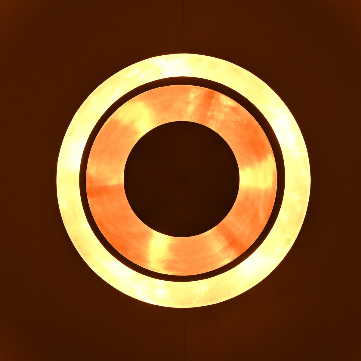 Bottom glowing ring view of layered brass disc chandelier illuminated with warm ambient lighting.