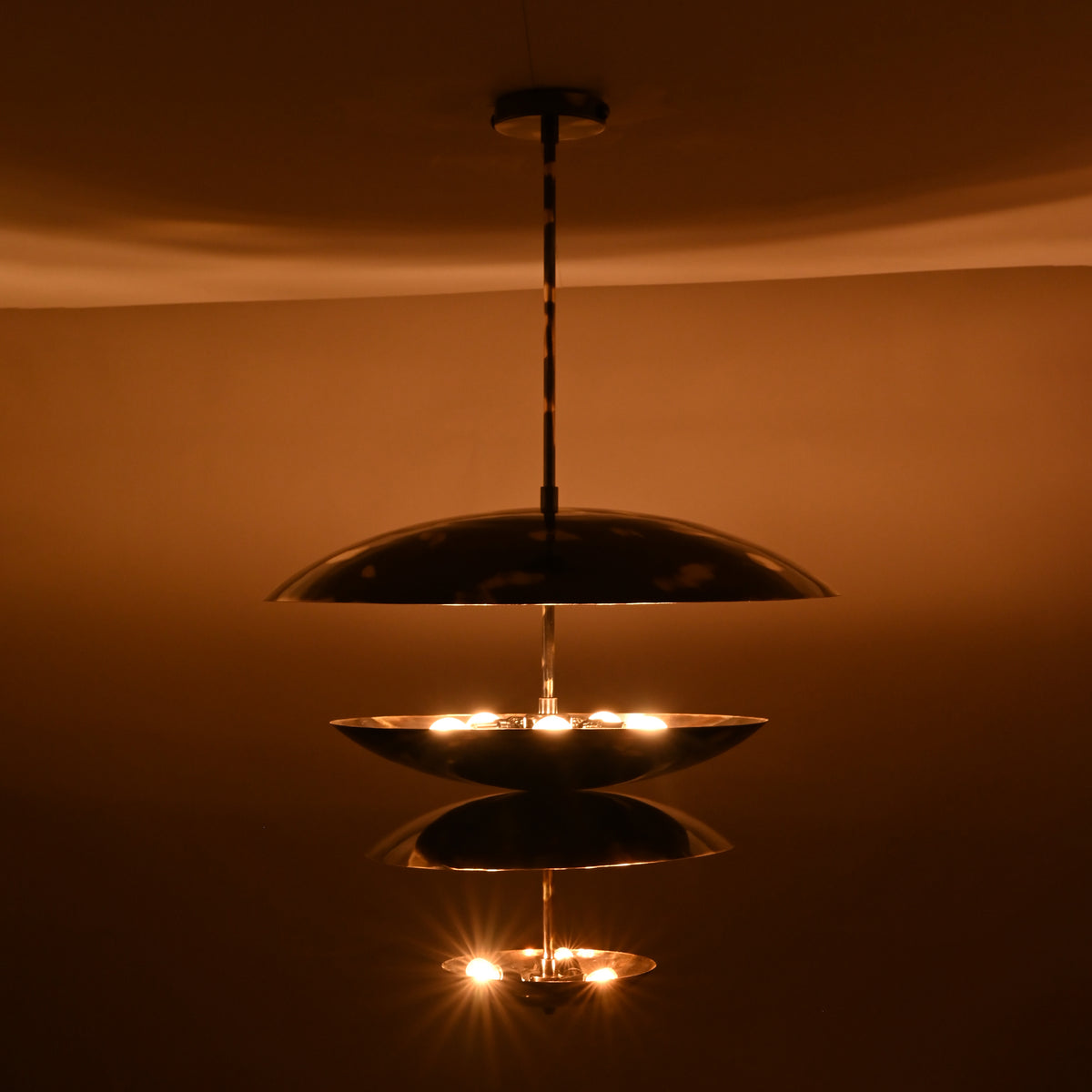 Illuminated brass multi-layer disc chandelier in a night setting showcasing glowing tiers