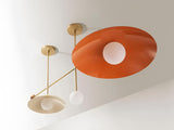 Close-up view of a handcrafted brass ceiling chandelier showcasing a large orange disc shade with frosted glass globe and refined modern detailing.