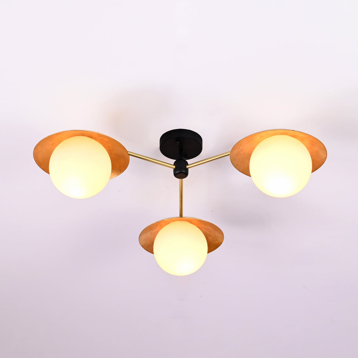 Angled view of handcrafted brass flush mount ceiling light featuring disc shades and opal glass globes.