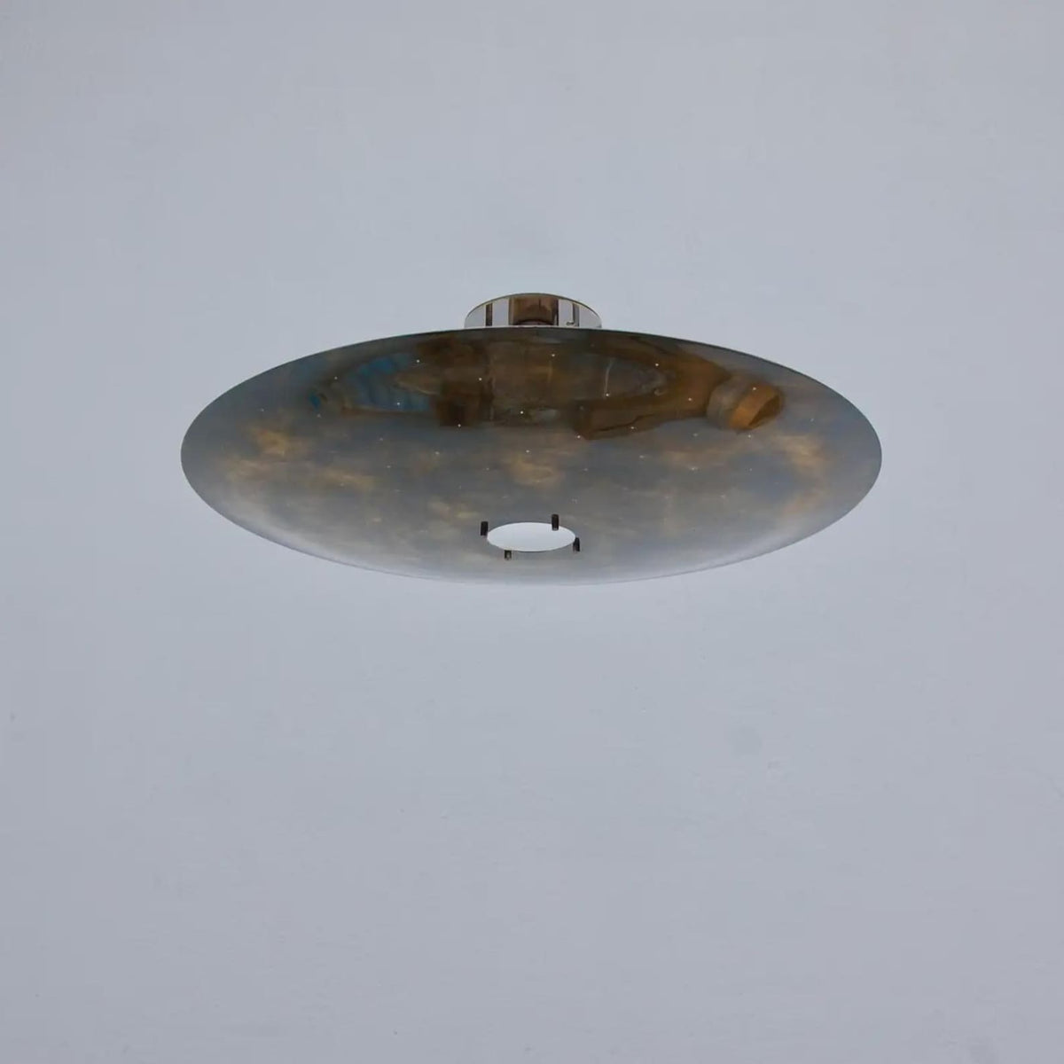 Minimalist brass disc flush mount ceiling light installed on ceiling, casting soft ambient indirect lighting with a refined industrial aesthetic.