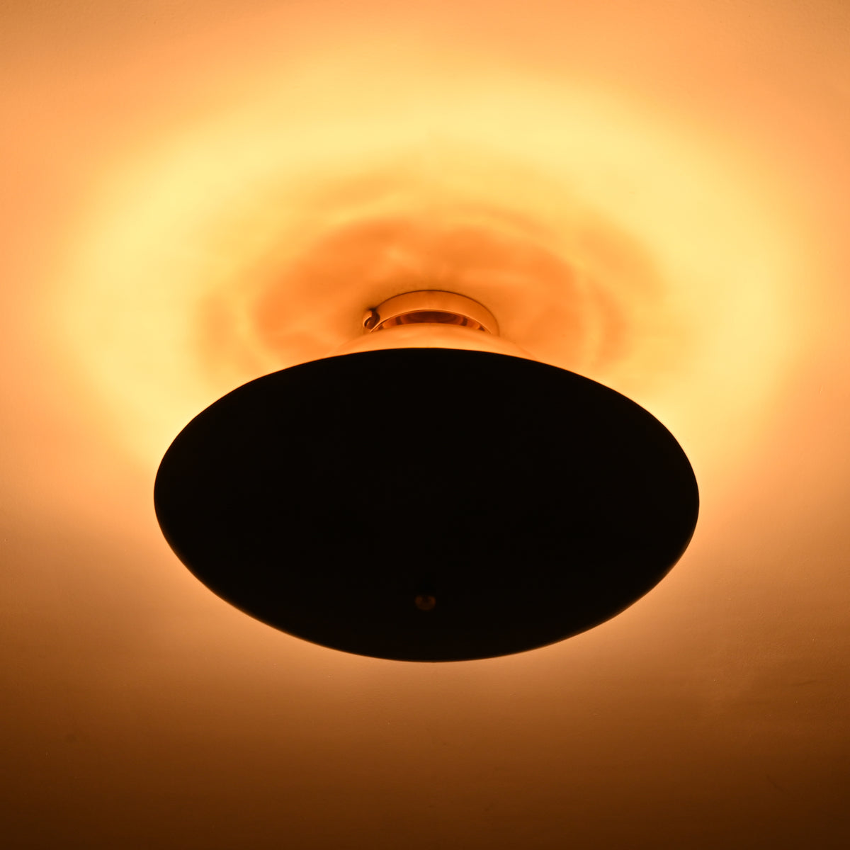 Mixed-finish brass flushmount in a dark room, showing strong warm halo lighting effect above the fixture.