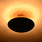 Mixed-finish brass flushmount in a dark room, showing strong warm halo lighting effect above the fixture.