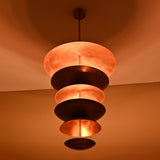 Angled nighttime view of multi-tier brass fountain chandelier radiating warm light across walls and ceiling