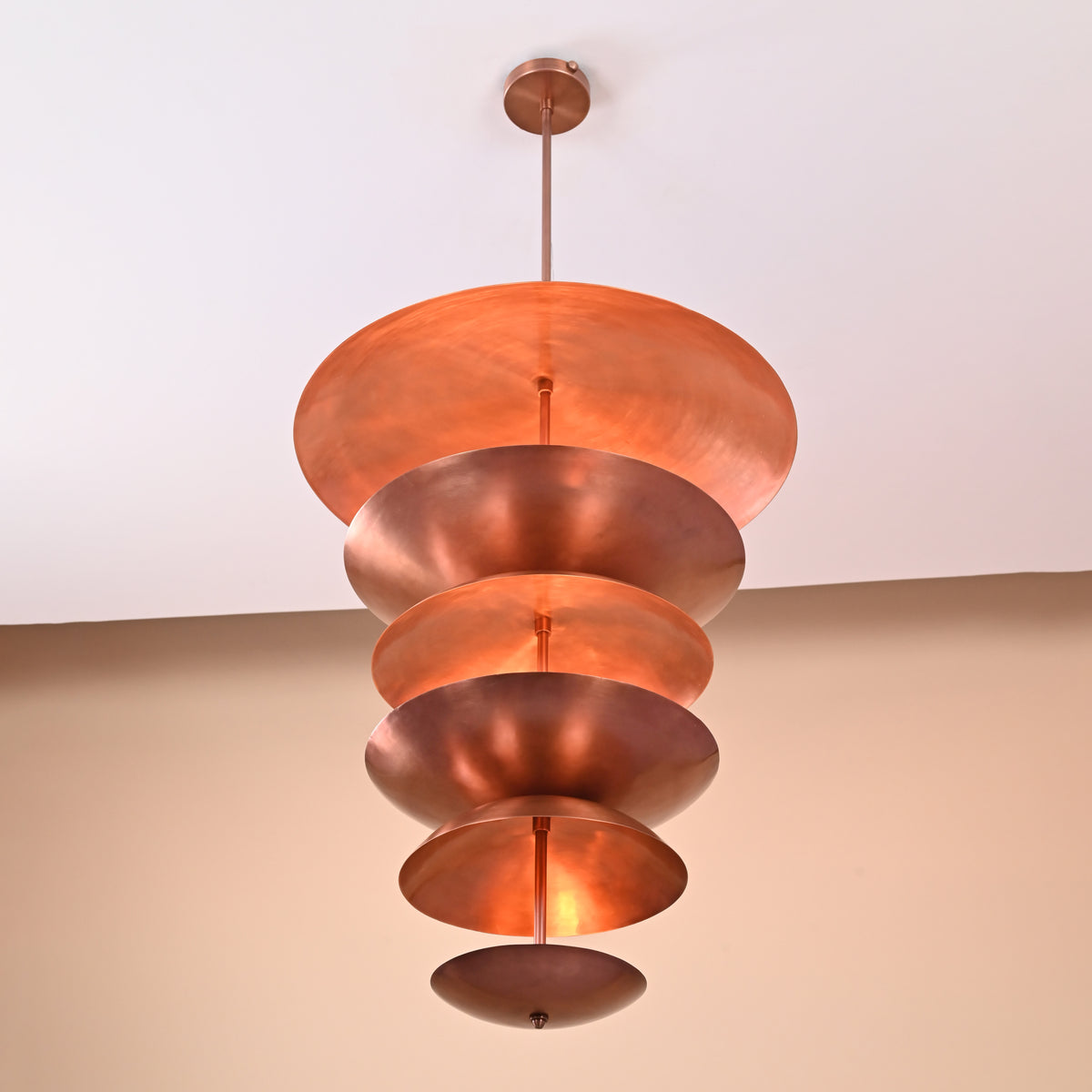 Underside view of copper brass disc chandelier showcasing circular layered discs with reflective metallic finish