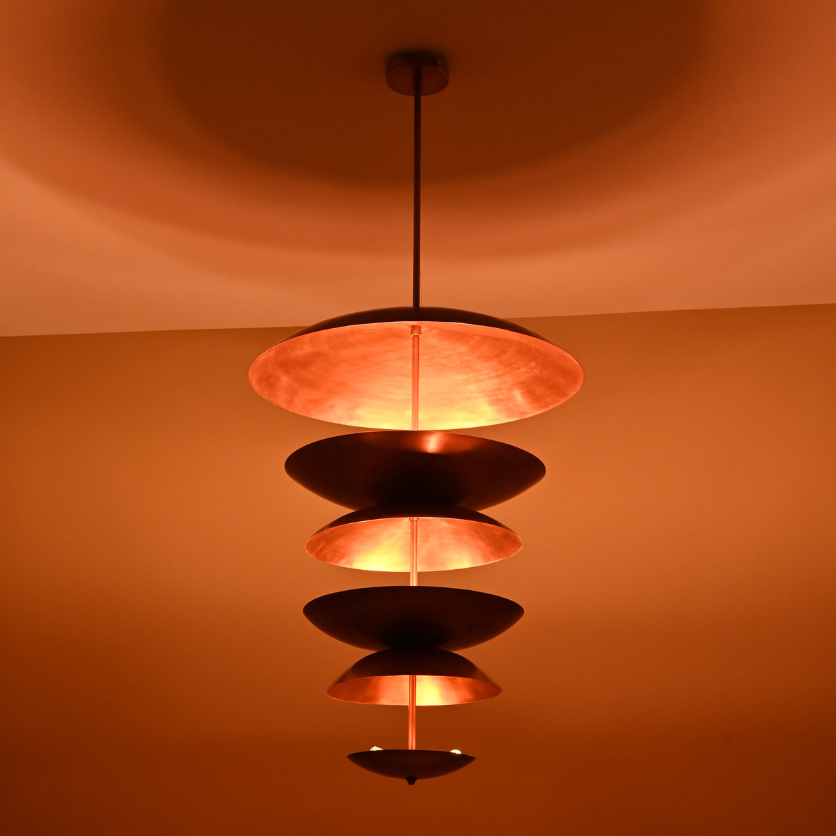 Side perspective of handcrafted brass disc chandelier under warm ambient lighting showing elegant cascading form