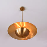 Underside view of raw brass pendant showing the glowing dome interior and circular light reflection pattern